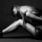 Side views of sad desperately young tied woman sitting on the floor on a gray background. Concept of addiction and fears. Place for advertising. Black and white photo